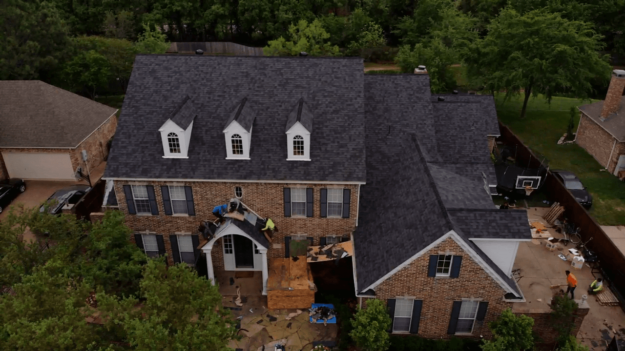 Aerial view of a two-storey brick home with dormer windows and a newly installed dark shingle roof