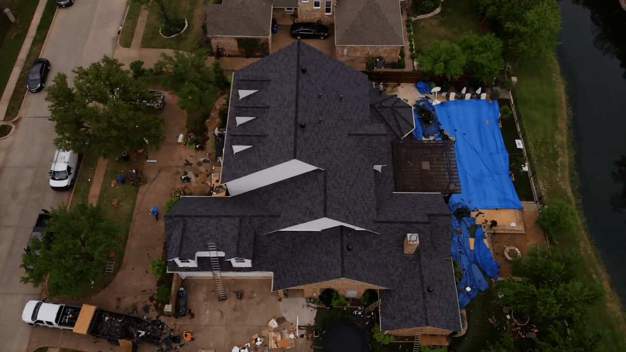 Aerial view of a roof replacement in progress, new dark shingles part-laid and blue tarps protecting the work area