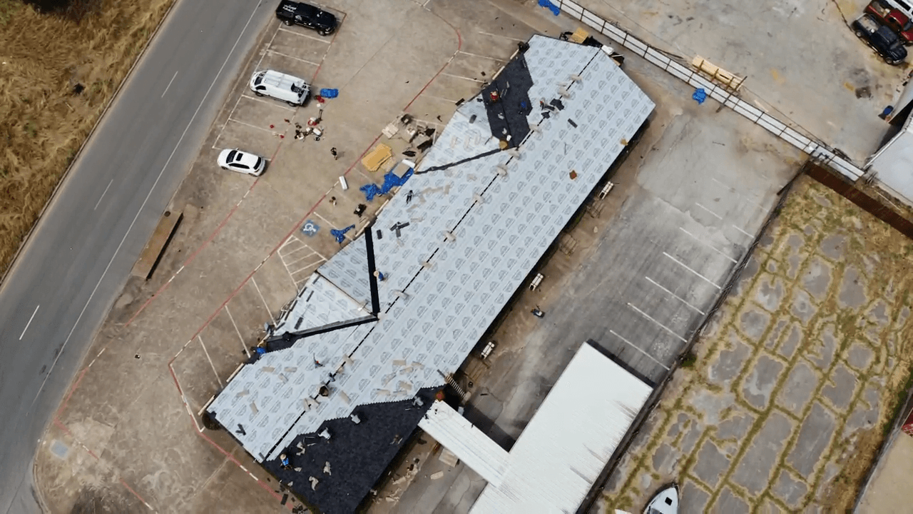 Aerial view of a crew re-roofing a long commercial building, fresh underlayment laid across the deck