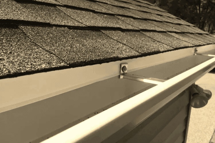 Close-up of a roof edge showing shingles, drip edge and gutter hangers