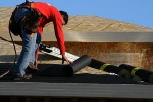 Roofer unrolling black felt underlayment across a low-slope roof deck