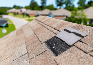 Close-up of damaged asphalt shingles on a roof ridge with the underlayment exposed beneath